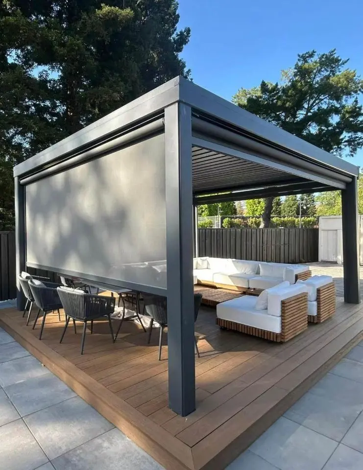 A modern outdoor patio in Scottsdale, AZ, boasts a pergola with adjustable louvers and custom patio covers. It features a large L-shaped sofa with white cushions and a dining area with black chairs, nestled amidst trees and a fenced yard on a sunny day.