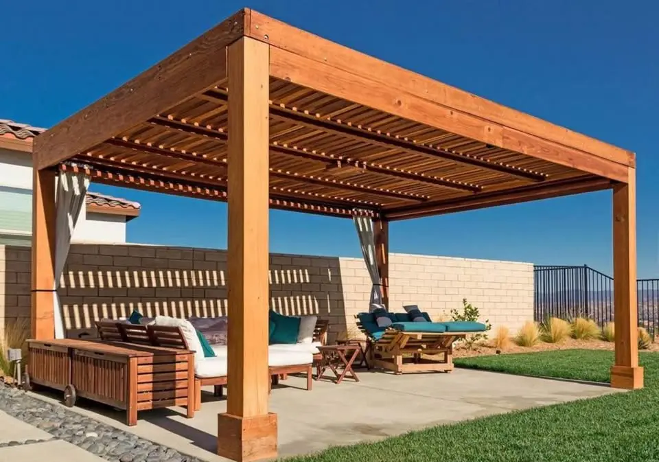 A custom patio cover made from wood stands over patio furniture, including a sofa, chairs, and a lounger, on a concrete patio. Green grass surrounds the area, and a clear blue sky is visible in the background. This serene space is enclosed by a brick wall in Scottsdale, AZ.